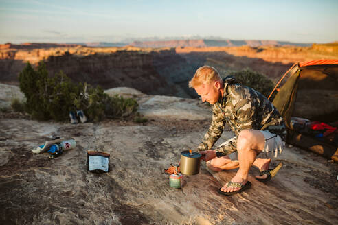 Männlicher Camper kocht Wasser mit einem Flüsterlicht im Camp in der Wüste - CAVF82508