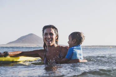 Lächelnde junge Mutter und Sohn spielen am Meer - CAVF82543