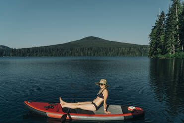 Eine junge Frau sitzt auf einem SUP auf dem Lost Lake in Oregon. - CAVF82561