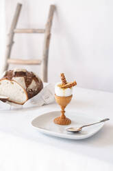 Zwei Cracker mit Sesam in einem zerbrochenen gekochten Ei auf einem Holzständer auf einem Tisch mit einem weißen Tischtuch - CAVF82683