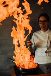 Female chef is making flambé in the restaurant kitchen - CAVF82697