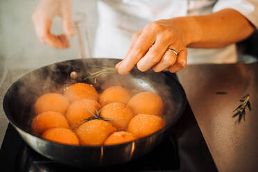 Hand eines Kochs, der Rosmarin zum Kochen in einer Bratpfanne hinzufügt Aprikosen - CAVF82698