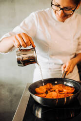 Female chef is adding water to cooking apricots - CAVF82700