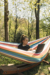 Junge Frau, die in der Hängematte sitzend im Garten am Laptop lernt - GUSF03798