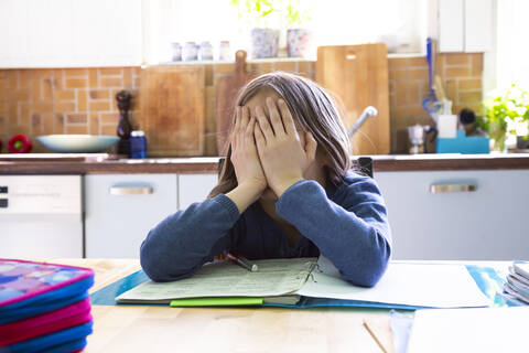 Girl doing homework in kitchen at home, hands on face stock photo