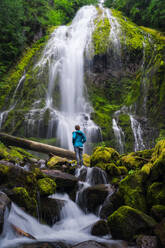 Junge Frau blickt auf einen riesigen Wasserfall im Wald - CAVF82823