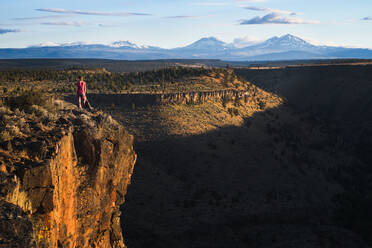 Frau steht am Rande einer Klippe mit Blick auf eine Schlucht und Berge - CAVF82824