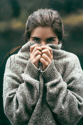 Porträt einer jungen Frau, die ihr Gesicht mit einem bequemen Pullover bedeckt - CAVF82835