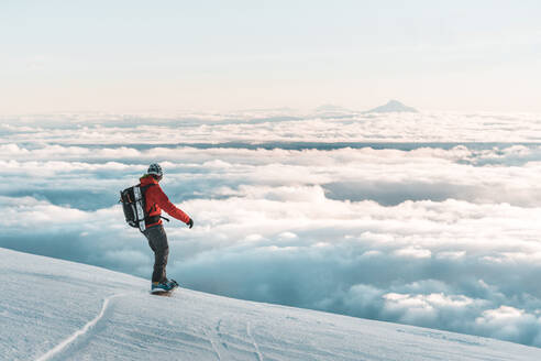 Snowboarder fährt bei Sonnenuntergang über den Wolken den Berg hinunter - CAVF82837