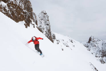 Snowboarder in roter Jacke fährt den Berg hinunter - CAVF82842