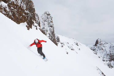 Snowboarder riding down mountain in red jacket - CAVF82842