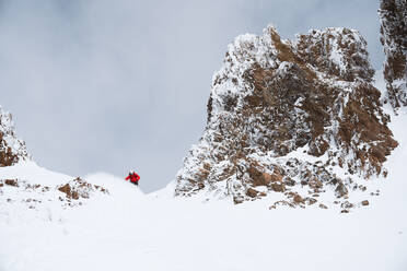 Snowboarder in roter Jacke macht eine Kurve in den Bergen - CAVF82844