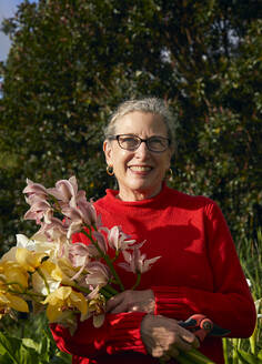 Ältere Frau hält Blumenstrauß mit frischen Schnittblumen in ihrem Garten - CAVF82865