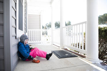 Wide View of Boy in Pink Snow Pants Sitting on Snowy Front Porch - CAVF82889