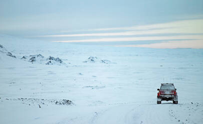 Red SUV driving through winter landscape in Iceland - CAVF82980