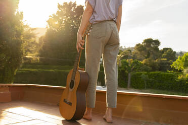 Rückansicht einer Frau mit Gitarre auf einer Terrasse bei Sonnenuntergang - AFVF06353