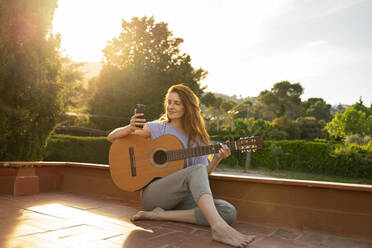 Rothaarige Frau spielt Gitarre auf Terrasse - AFVF06354