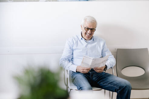 Älterer Mann sitzt im Wartezimmer einer Arztpraxis und liest ein Faltblatt - DAWF01528