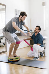 Physiotherapist assisting patient, practicing on balance trainer - DAWF01572