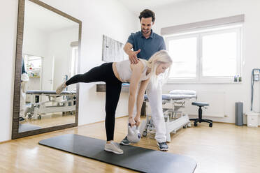 Physiotherapeutin hilft einer Patientin, die auf einer Gymnastikmatte balanciert - DAWF01575
