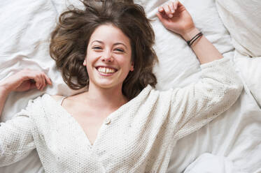Cheerful young woman lying in bed at home - DIGF12161