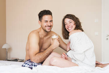 Glückliches junges Paar sitzt zu Hause auf dem Bett - DIGF12176