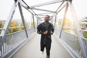 Young man with headphones jogging on footbridge - DIGF12228