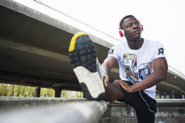 Young jogger stretching his leg and listening to music in the city - DIGF12248