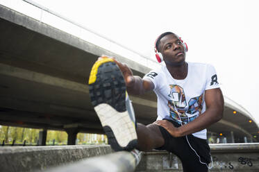 Young jogger stretching his leg and listening to music in the city - DIGF12249