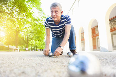Älterer Boule-Spieler kniend auf dem Boden - DIGF12258