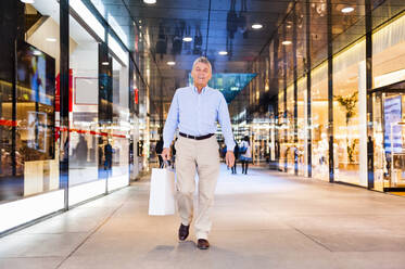 Portrait of happy senior man with shopping bag in a shopping center - DIGF12260
