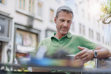 Älterer Mann, der ein Smartphone benutzt, während er in einem Straßencafé sitzt - DIGF12266