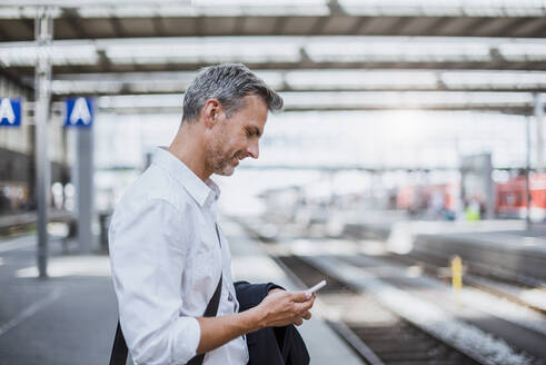 Geschäftsmann, der ein Smartphone benutzt, während er am Bahnsteig steht - DIGF12270