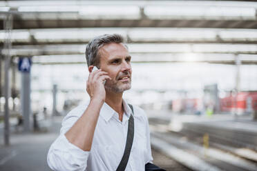 Geschäftsmann, der über sein Smartphone spricht und wegschaut, während er am Bahnsteig steht - DIGF12271