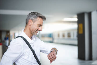 Businessman checking time while sitting at railroad station platform - DIGF12275