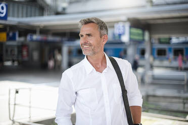 Smiling businessman looking away while standing at railroad station - DIGF12279