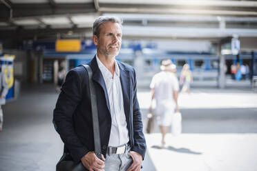 Lächelnder Geschäftsmann, der wegschaut, während er am Bahnhof steht - DIGF12280