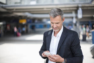 Geschäftsmann, der ein Smartphone benutzt, während er am Bahnhof steht - DIGF12281