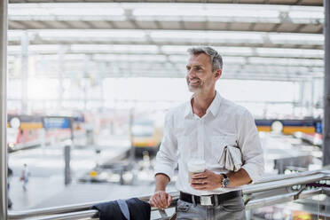 Nachdenklicher Geschäftsmann mit Kaffee in der Hand, der wegschaut, während er am Geländer steht - DIGF12289