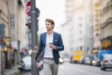 Portrait of young businessman with newspaper and coffee to go walking on the street - DIGF12302