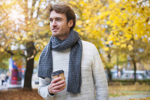 Portrait of young man with coffee to go in autumn - DIGF12311