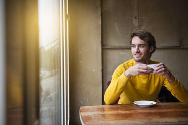 Porträt eines jungen Mannes in einem Café mit Blick aus dem Fenster - DIGF12315