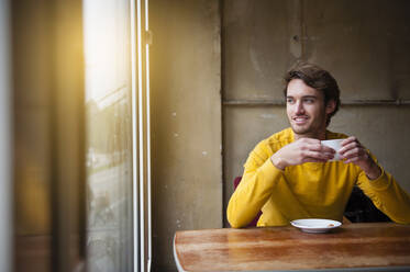 Portrait of young man in a coffee shop looking out of window - DIGF12315