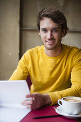 Porträt eines jungen Mannes mit digitalem Tablet in einem Café - DIGF12317