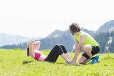 Pärchen bei Situps auf einer Wiese, Wallberg, Bayern, Deutschland - DIGF12354