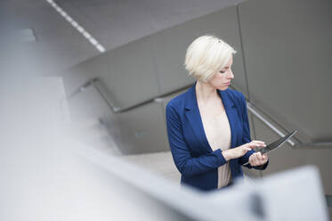 Porträt einer lächelnden blonden Geschäftsfrau, die auf einer Treppe ein Tablet benutzt - DIGF12364