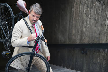 Geschäftsmann, der ein Fahrrad trägt, während er eine Treppe hinaufsteigt - DIGF12371