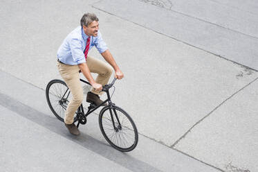 Lächelnder Geschäftsmann fährt Fahrrad auf der Straße in der Stadt - DIGF12374
