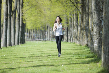 Confident young woman looking away while running on grassy land in park - DIGF12387