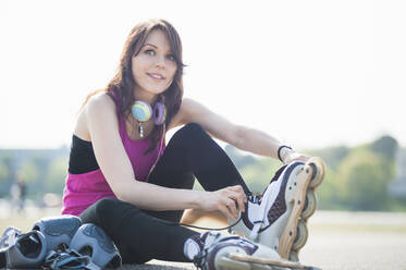 Smiling confident young woman wearing inline skates while sitting against clear sky in park - DIGF12391